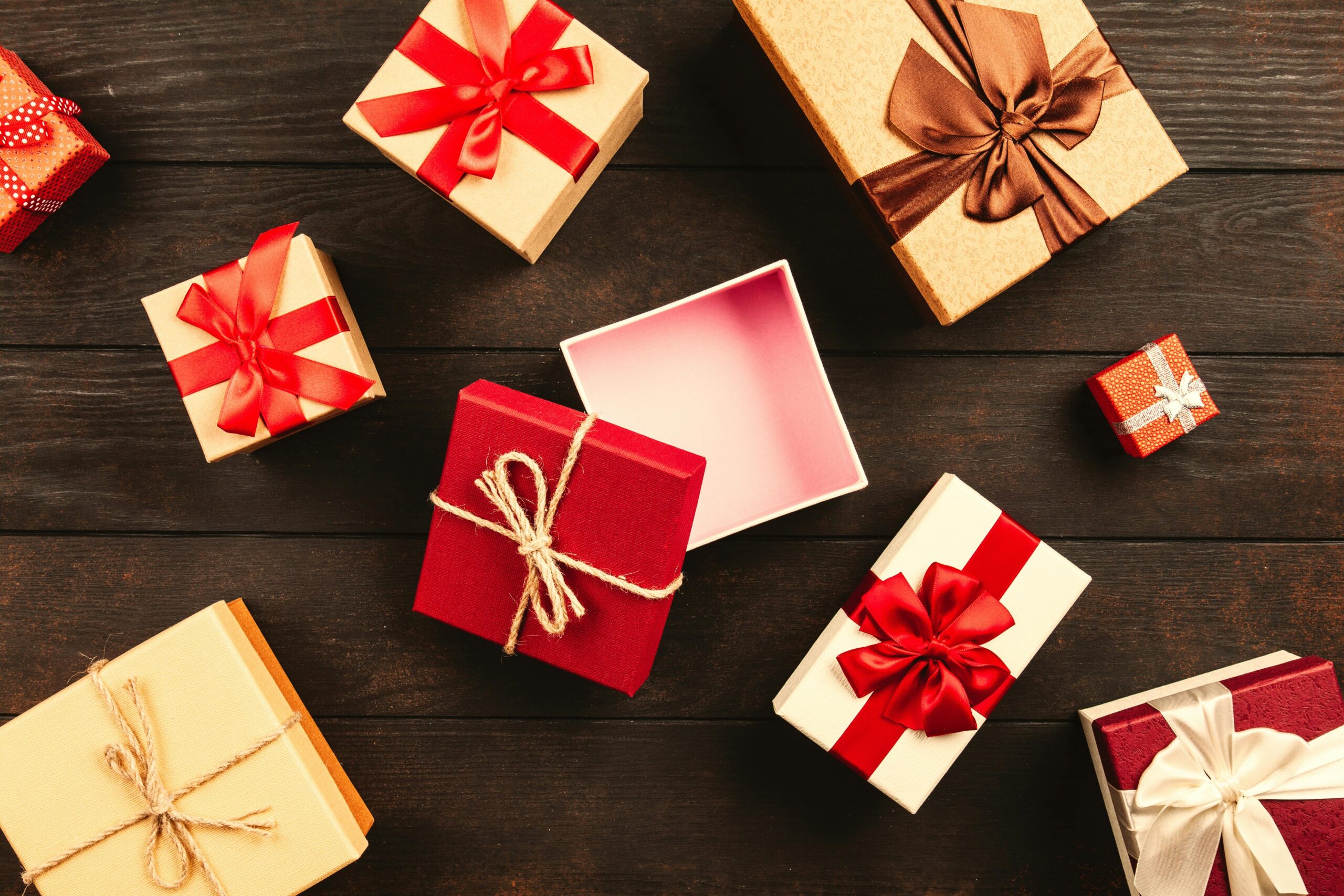A festive flat lay of various Christmas presents adorned with colorful ribbons on a wooden background.