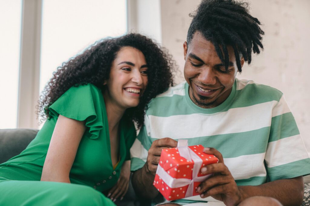 A happy interracial couple enjoys a gift exchange at home, capturing a moment of joy and connection.
